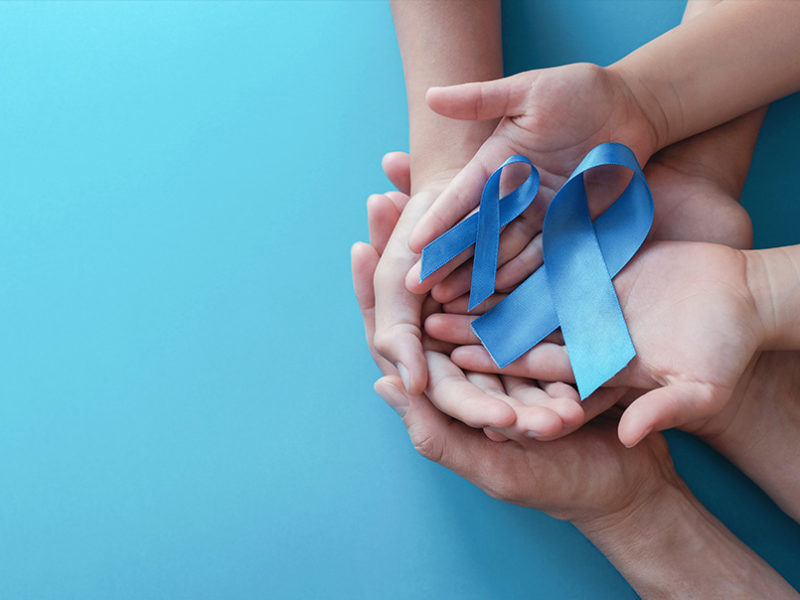 A group of hands holding two blue awareness ribbons