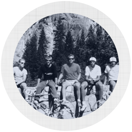 A group of men sitting on a stone wall with their bicycles