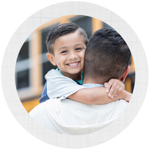 A young boy smiling and being held by his father